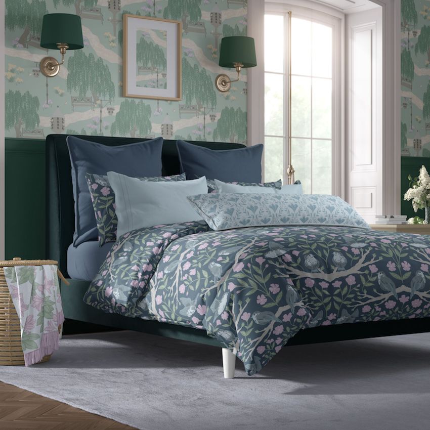 Cottage style bedroom bedding mockup featuring a bed with blue and floral patterned linens, green wallpaper, and wall sconces.