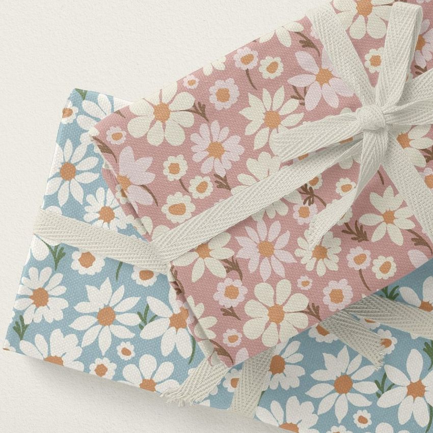 Folded fabrics mockup showing two bundles tied with cream ribbons, featuring daisy patterns on pink and blue backgrounds.