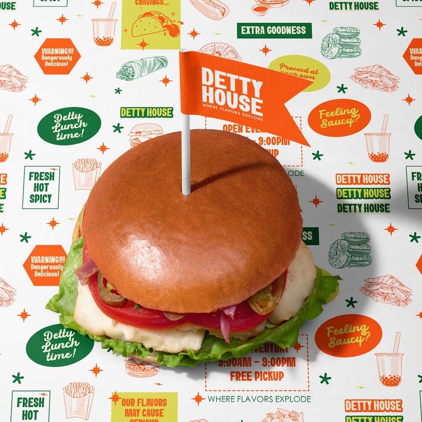 Burger mockup on branded wrapping paper with colorful text and icons, viewed from above under bright lighting.