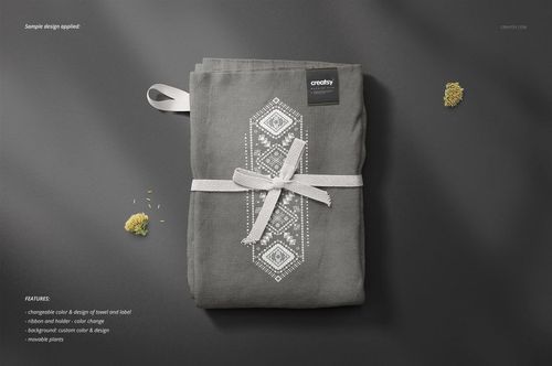 Folded gray kitchen towel mockup featuring a white geometric design, ribbon accent, and minimal props on a dark background.