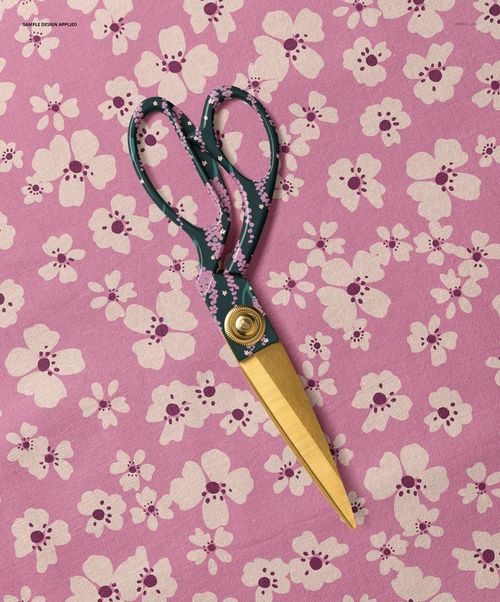 Top view of patterned scissors placed on pink cotton fabric with white floral motifs, shown in a PSD mockup scene.