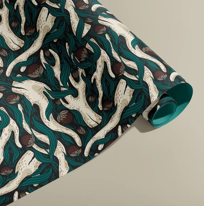 Gift wrapping paper mockup showing a rolled sheet with a teal, cream, and brown horns and flowers pattern on a neutral surface.