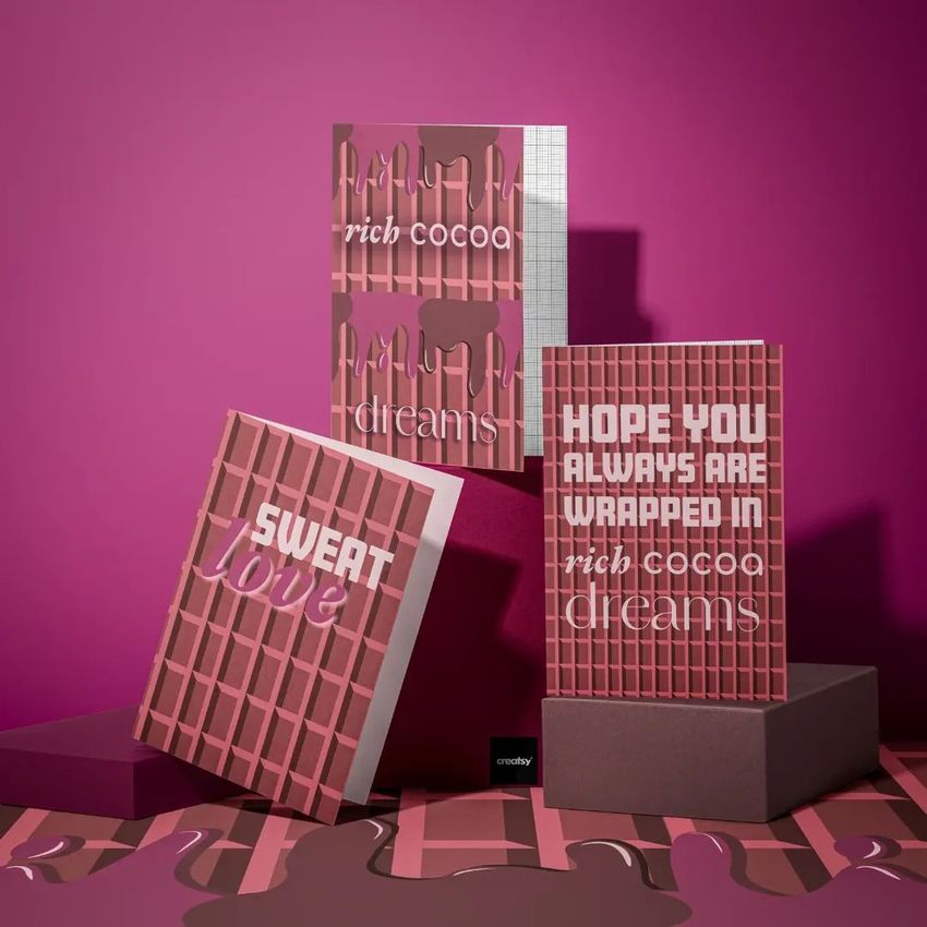 Greeting card mockup set featuring three cards with chocolate bar patterns and bold text, arranged on burgundy boxes against a pink background.