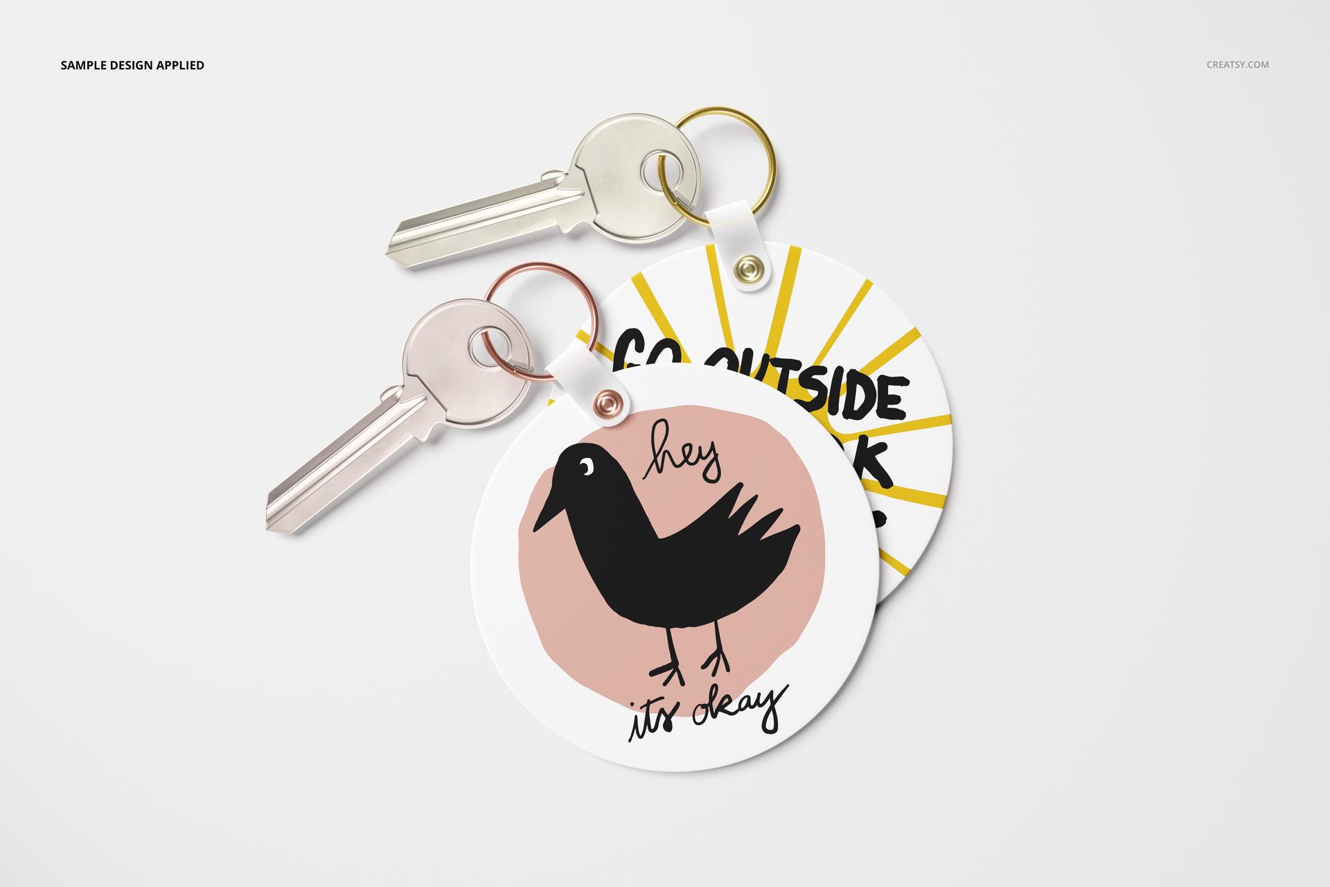 Round key tag mockup featuring two tags, one with a bird drawing and text, one with yellow sun rays and black lettering.