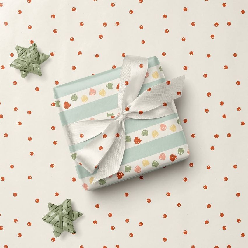 Square gift box mockup with pastel candy-themed wrapping paper and white ribbon, placed on a polka dot surface with two woven star ornaments.
