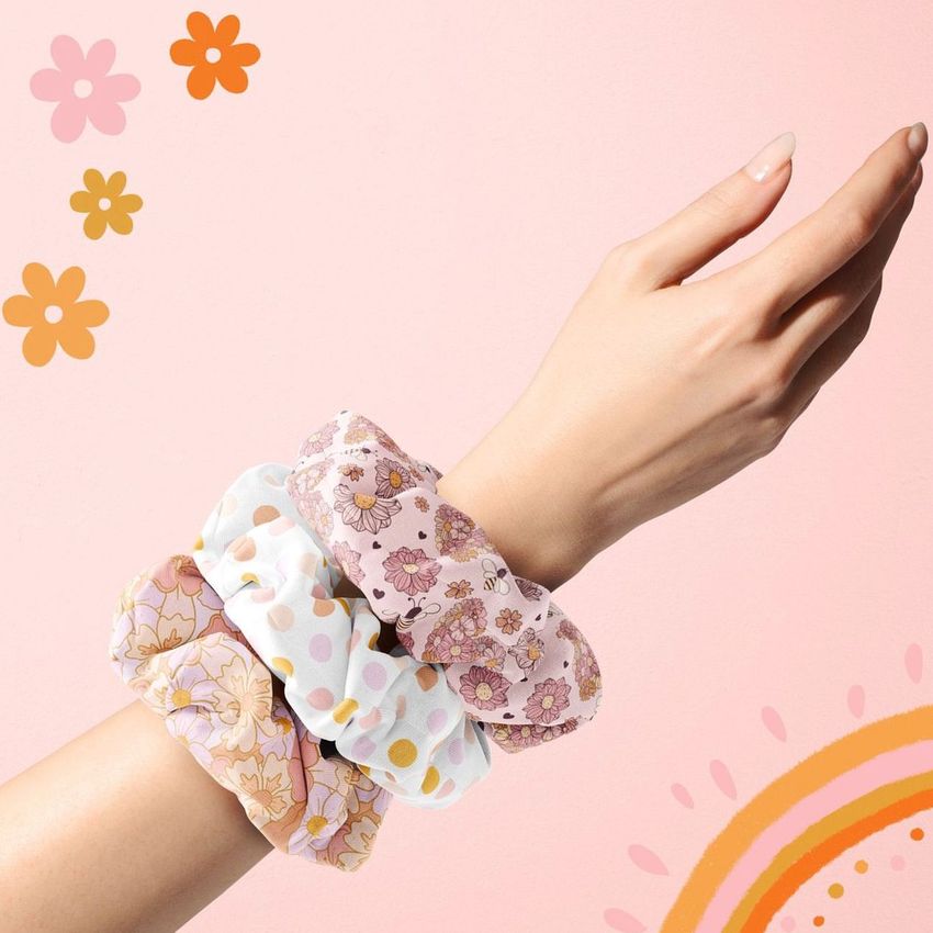 Fashion accessory mockup featuring a hand displaying pastel scrunchies, surrounded by decorative flower and sunburst shapes.