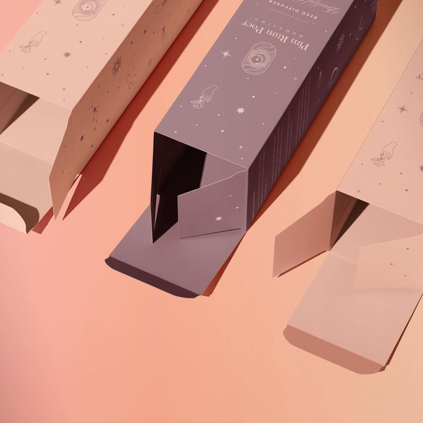 Tall box mockup featuring three pastel-colored packaging boxes with celestial patterns, shown from an angled top view on a pink surface.