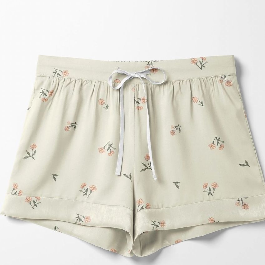 Silk pajama shorts mockup featuring a light cream fabric with a delicate pink floral pattern, shown from above on a white background.