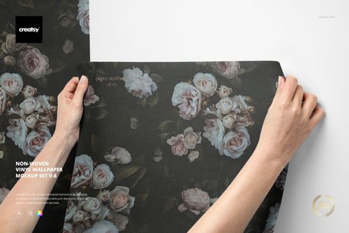 Top view of two hands unfolding a floral-patterned non-woven vinyl wallpaper mockup on a plain white background.