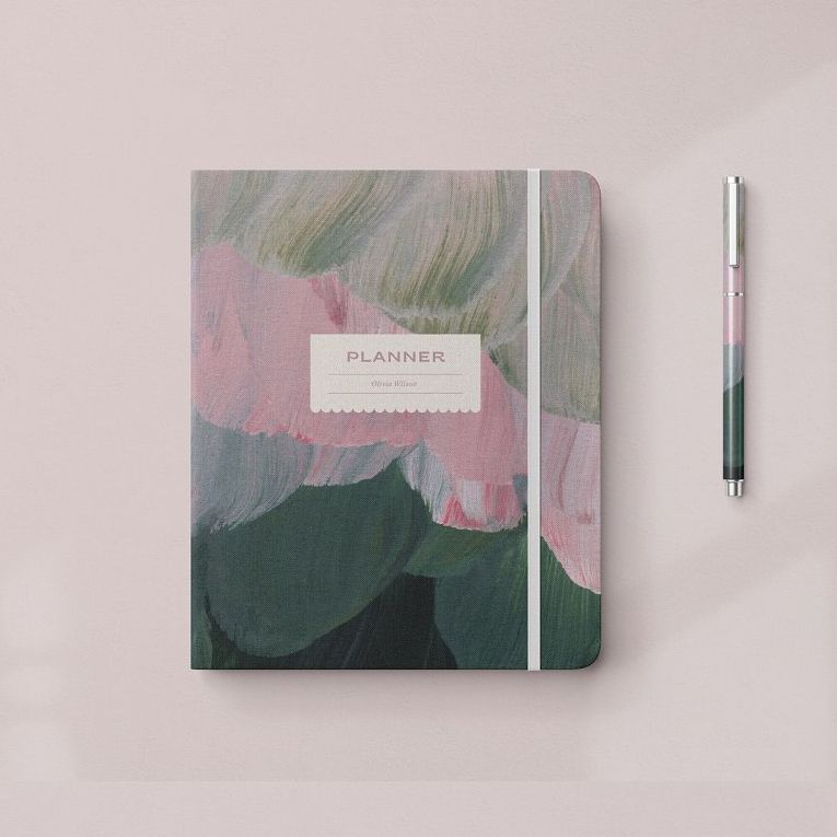 Stationery mockup featuring a closed planner with an abstract floral cover design and matching pen on a light pink surface.