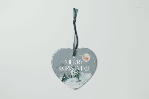 Heart-shaped ceramic Christmas ornament mockup with snowy pine trees and moon design, front view on white background.