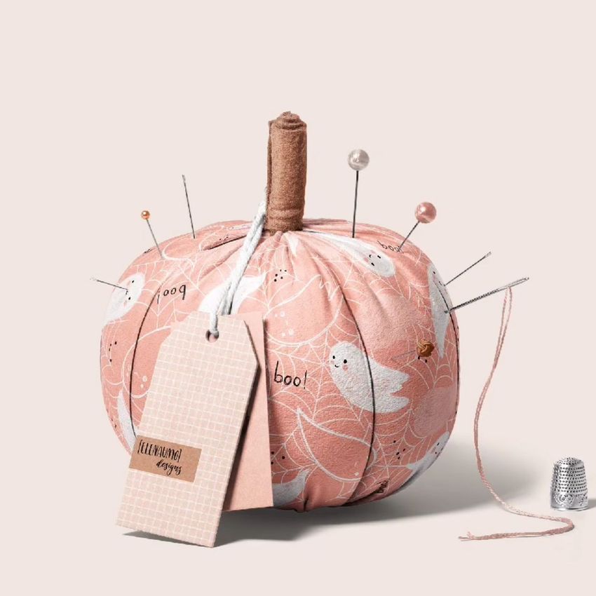 Fabric pumpkin mockup featuring a soft pink pumpkin with a white ghost pattern, pins, and a blank tag on a neutral background.