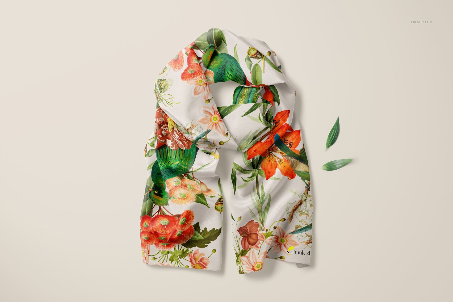 Crepe de Chine silk scarf mockup featuring botanical prints, shown folded with scattered green leaves nearby.