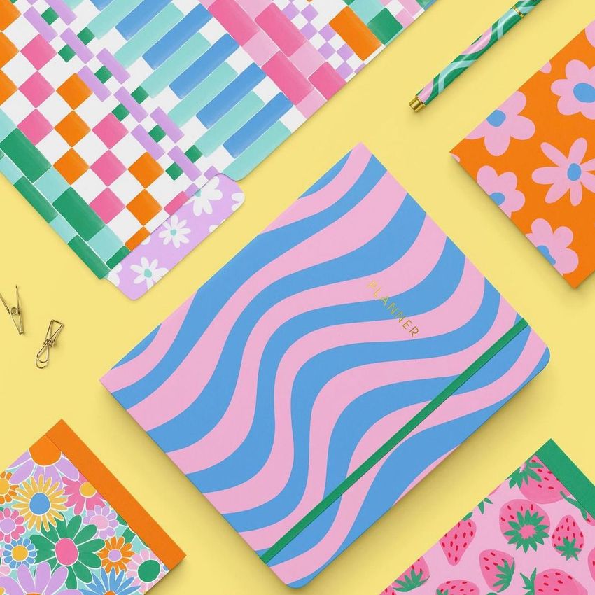 Stationery set mockup featuring colorful notebooks with bold patterns, a striped pencil, and binder clips on a yellow background.