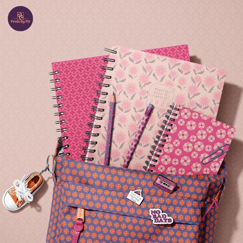 School backpack mockup with three spiral notebooks and pens in pink and purple patterns, viewed from above on a patterned background.