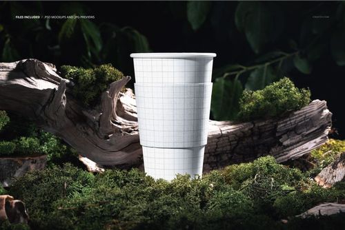 Paper cup mockup with grid pattern standing upright on mossy forest ground, surrounded by tree bark and green foliage.