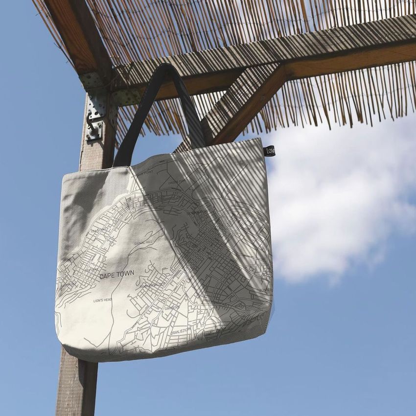 Natural cotton tote bag mockup hanging outdoors, featuring a detailed street map design in black on a light fabric background.
