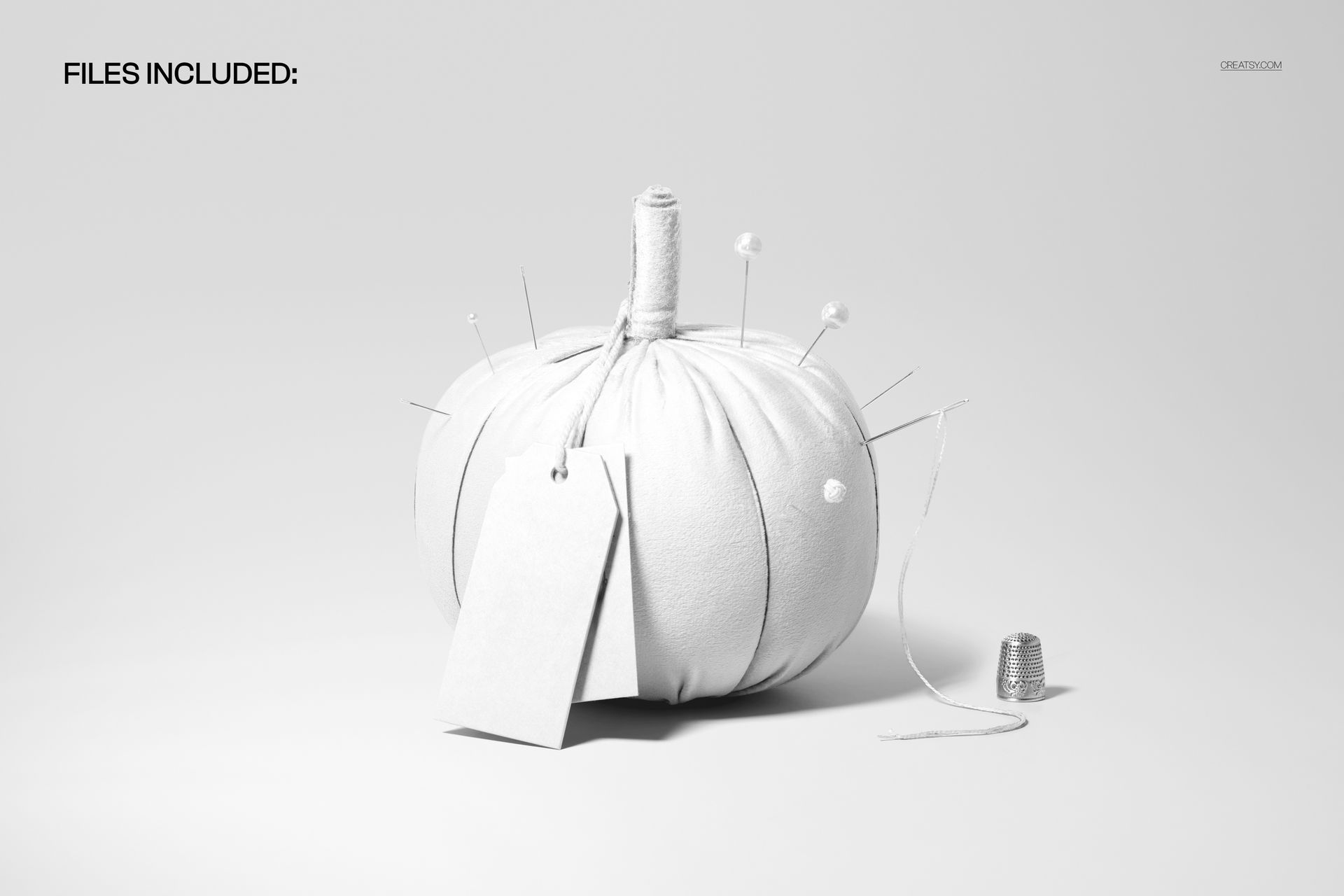 Front view of a fabric pumpkin mockup with sewing pins, blank label, thread spool, and thimble on a white background.