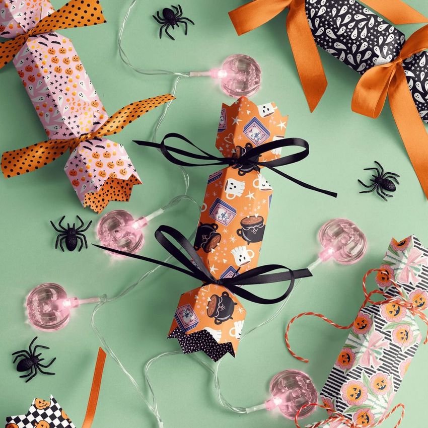 Halloween party cracker packaging mockup featuring colorful crackers with festive patterns, black bows, and plastic spiders on a green background.