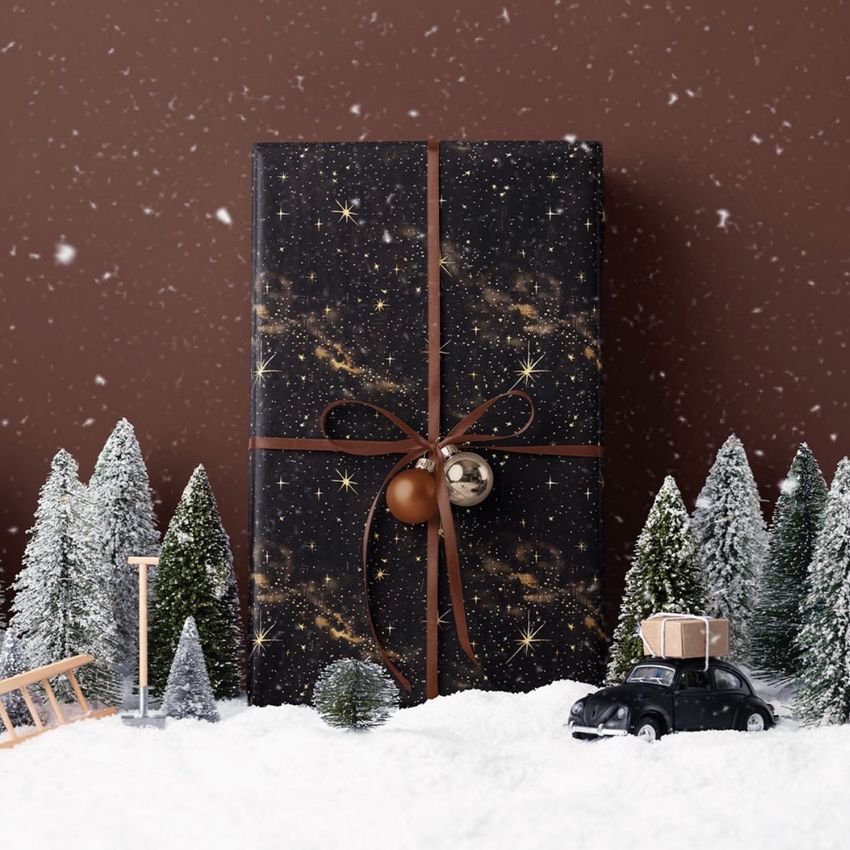 Christmas gift mockup featuring a black box with gold star pattern, tied with brown ribbon, surrounded by snow and miniature trees.