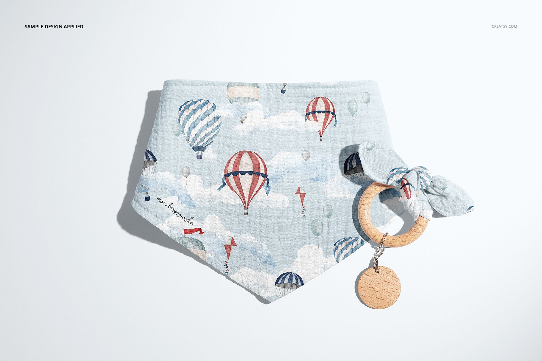 Front view of a baby muslin bandana mockup featuring a playful balloon and cloud print, paired with a wooden teether.