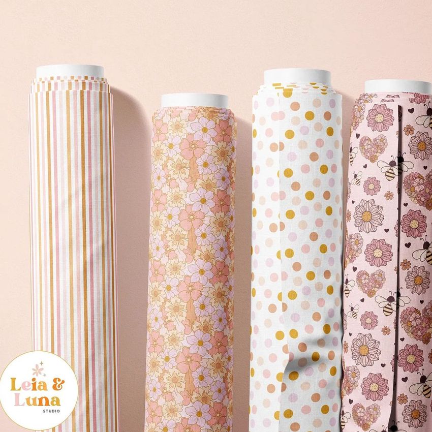 Fabric rolls mockup showing four upright rolls with pastel patterns, including stripes, florals, polka dots, and bees, against a pale background.