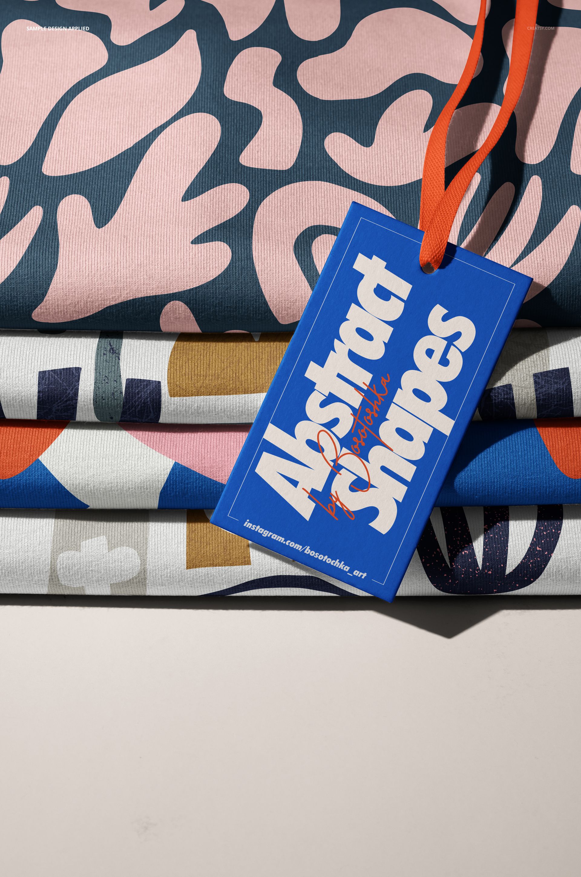 Front perspective of stacked jersey fabric mockup featuring colorful patterns and a blue tag reading 'Abstract Shapes'.