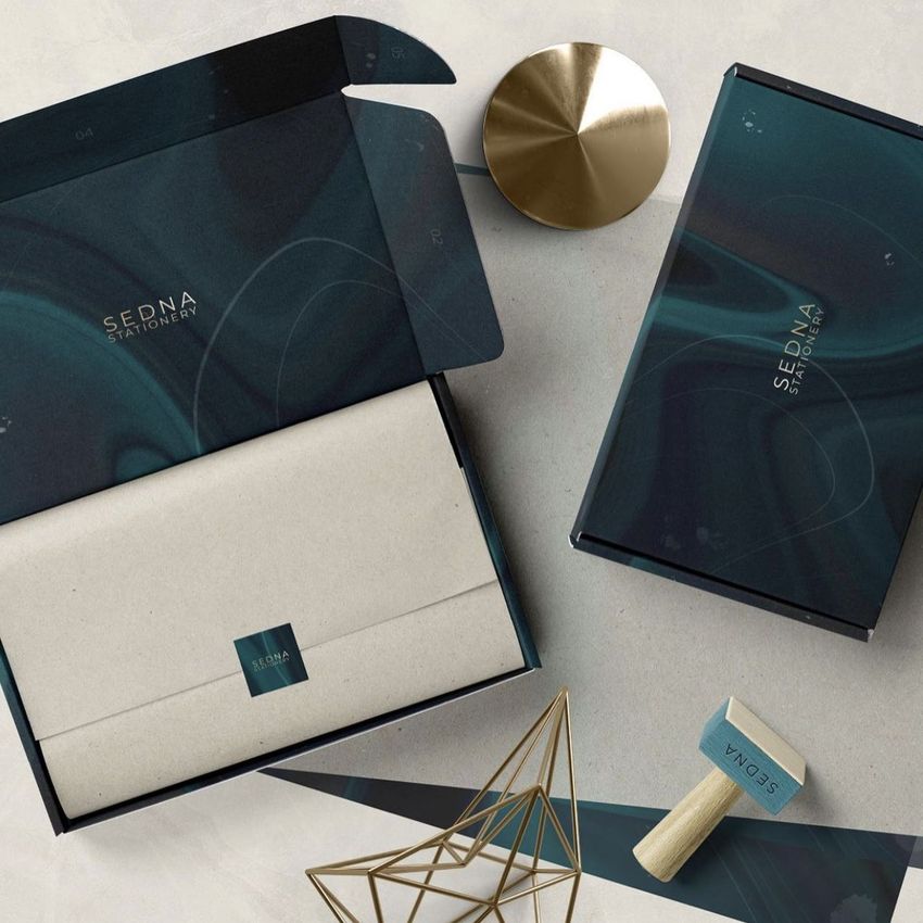 Mailing box mockup set featuring two dark blue boxes with abstract patterns, shown with envelopes and a custom stamp on a beige surface.