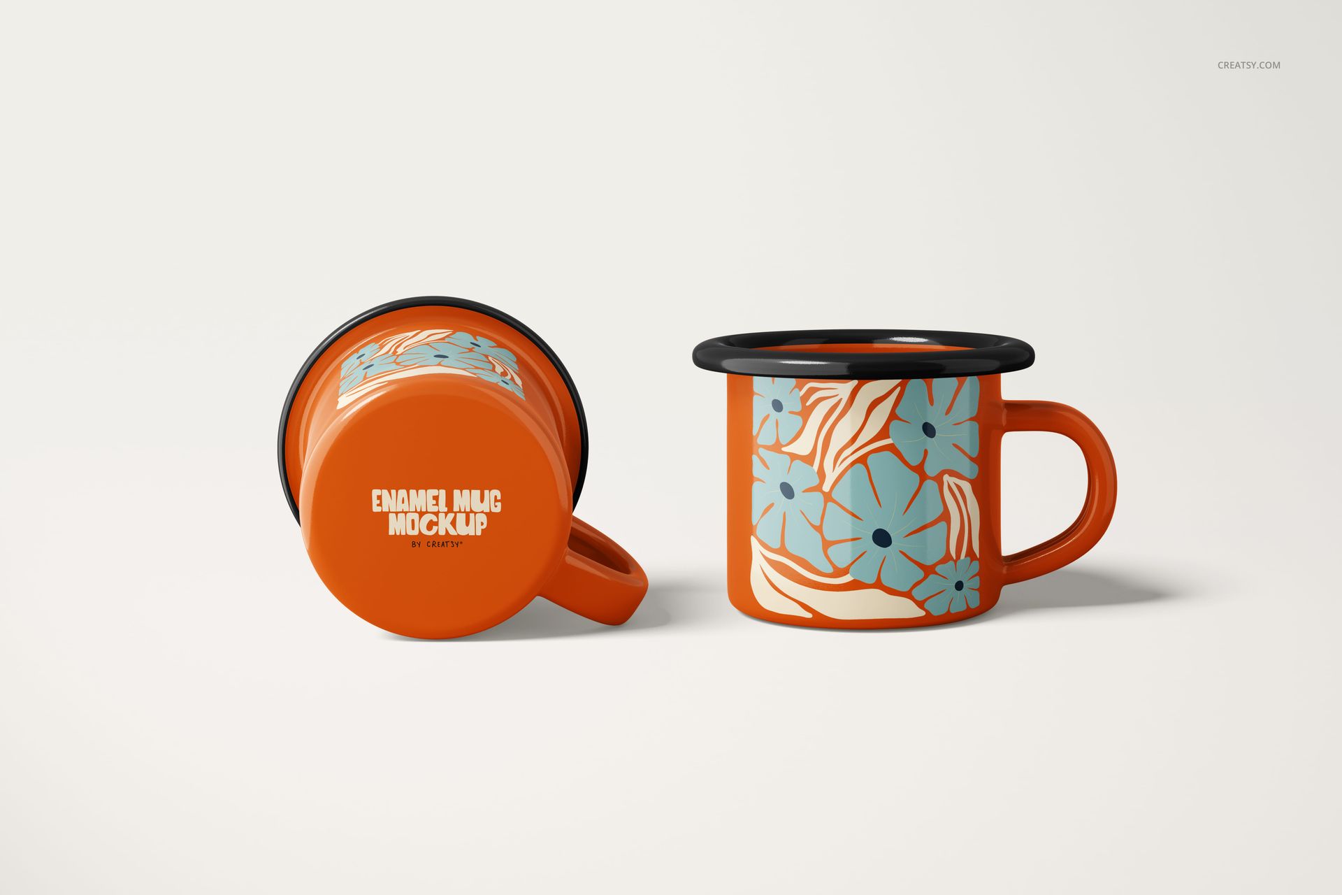 Two orange enamel mugs with black rims, one upright and one on its side, featuring a blue floral pattern on a white background.