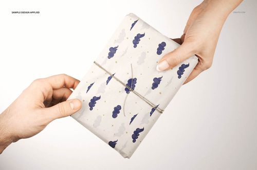 Hands holding a rectangular gift wrapped in white tissue paper with blue cloud and star patterns, viewed from above.