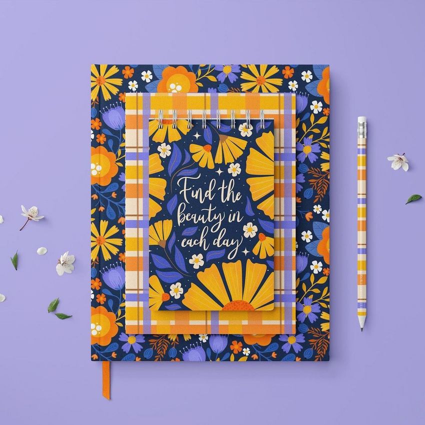 Stationery set mockup featuring a spiral notebook, hardcover book, and pencil with floral patterns on a purple background.