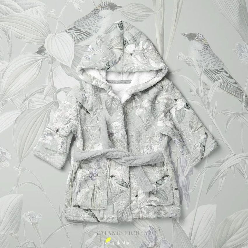 Baby bath dressing gown mockup with a botanical pattern, displayed flat against a matching floral and bird wallpaper background.
