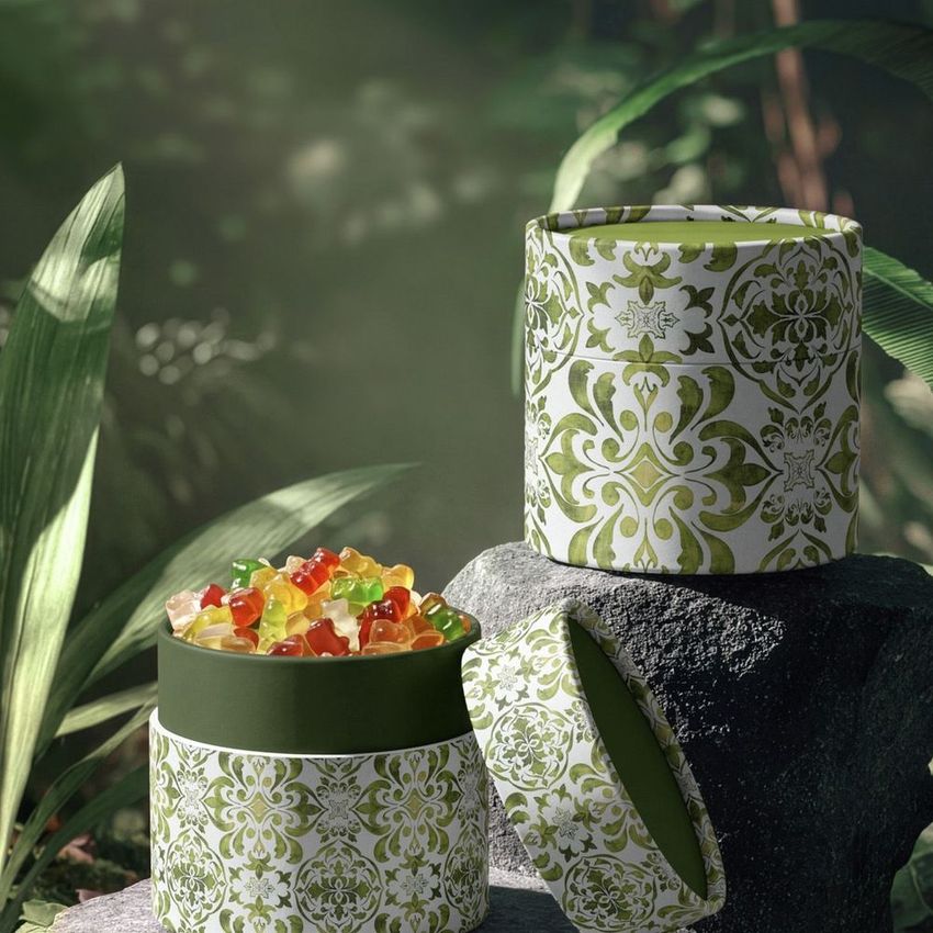 Paper tube packaging mockup featuring a decorative green and white pattern, filled with colorful jelly candies, set in a lush jungle scene.