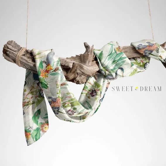 Silk scarf mockup draped over a piece of driftwood, featuring a botanical pattern with soft green and yellow tones.