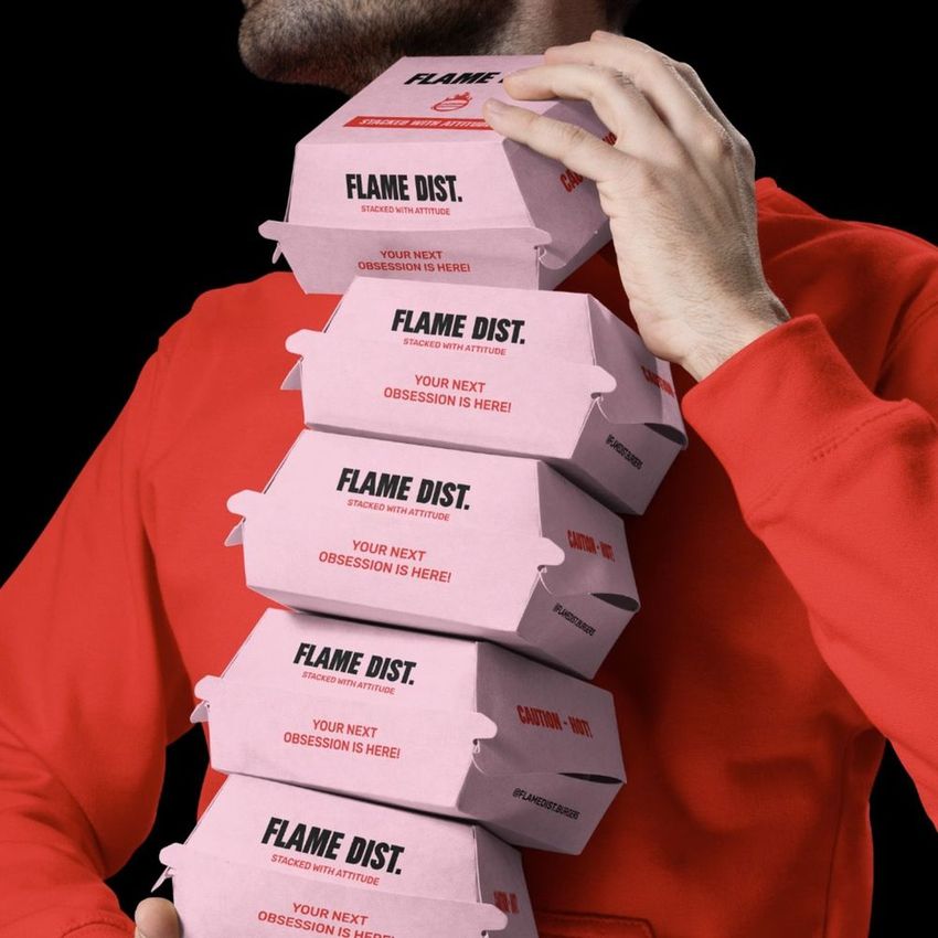 Burger boxes mockup showing a person in a red hoodie holding a tall stack of pink packaging with bold text on a black background.