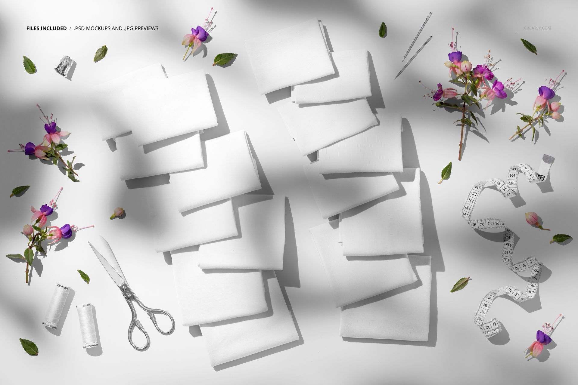 Jersey fabric mockup with multiple folded white fabric pieces arranged on a flat surface, surrounded by sewing tools and floral decorations.