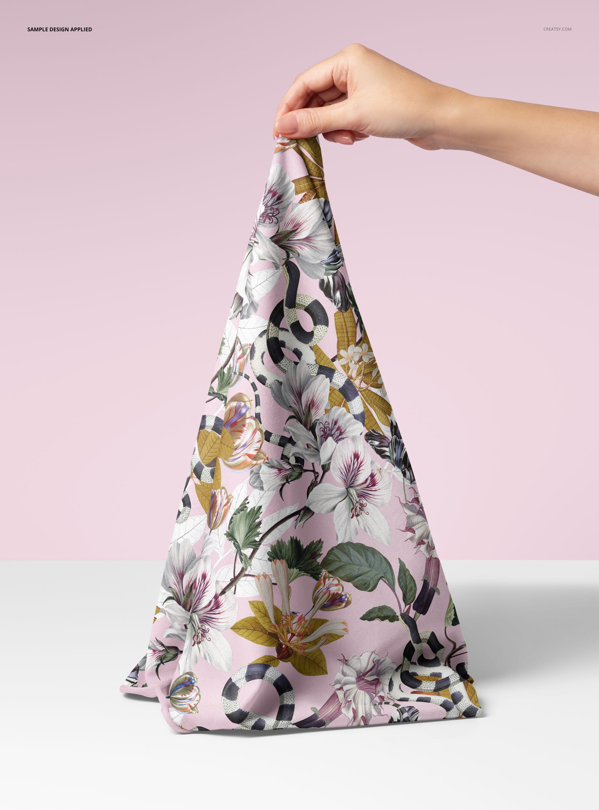 PSD mockup showing a human hand grasping floral jersey fabric with botanical design, set before a pink wall.