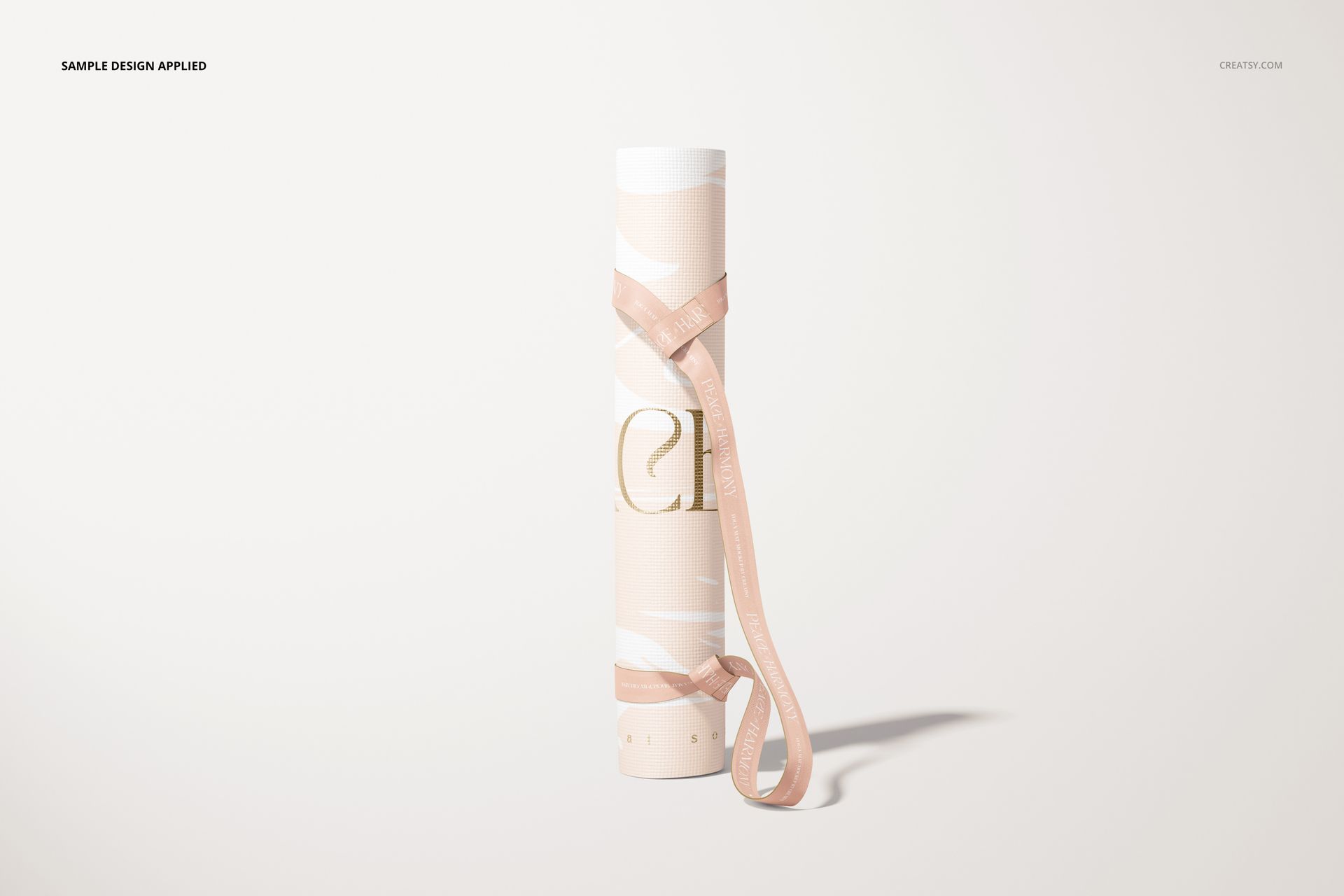 Yoga mat mockup featuring a rolled mat with soft pink and white design, shown upright with a pink carrying strap.