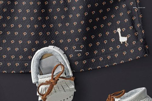 Front view of a baby dress mockup with a dark textured fabric featuring a small repeating pattern and white llama motif.