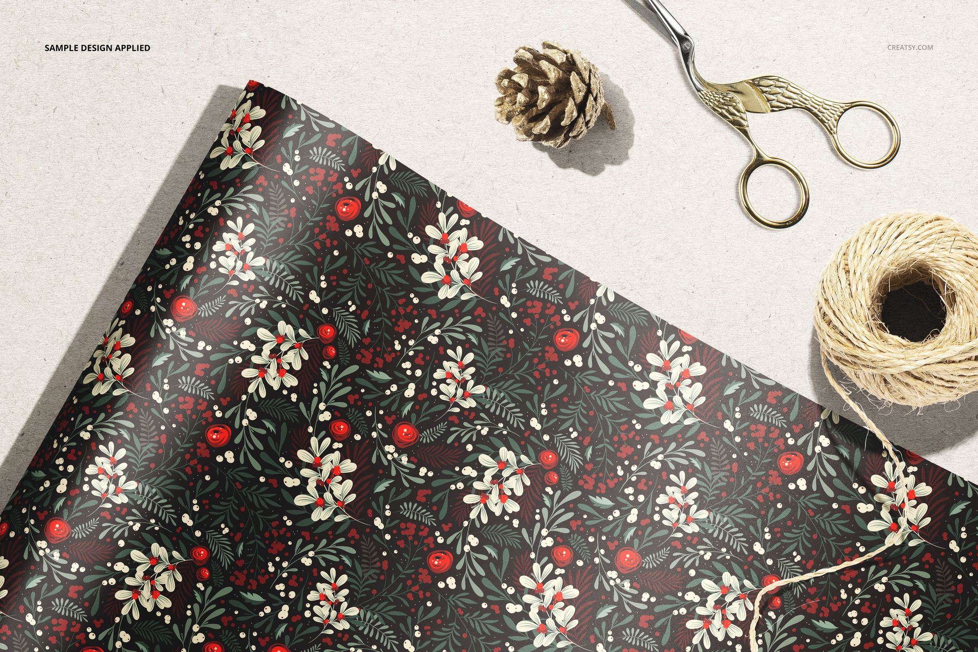 Close-up of wrapping paper mockup featuring a botanical design, with scissors, twine, and pinecone nearby.