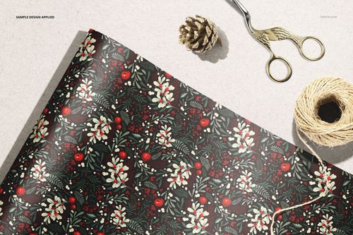 Close-up of wrapping paper mockup featuring a botanical design, with scissors, twine, and pinecone nearby.