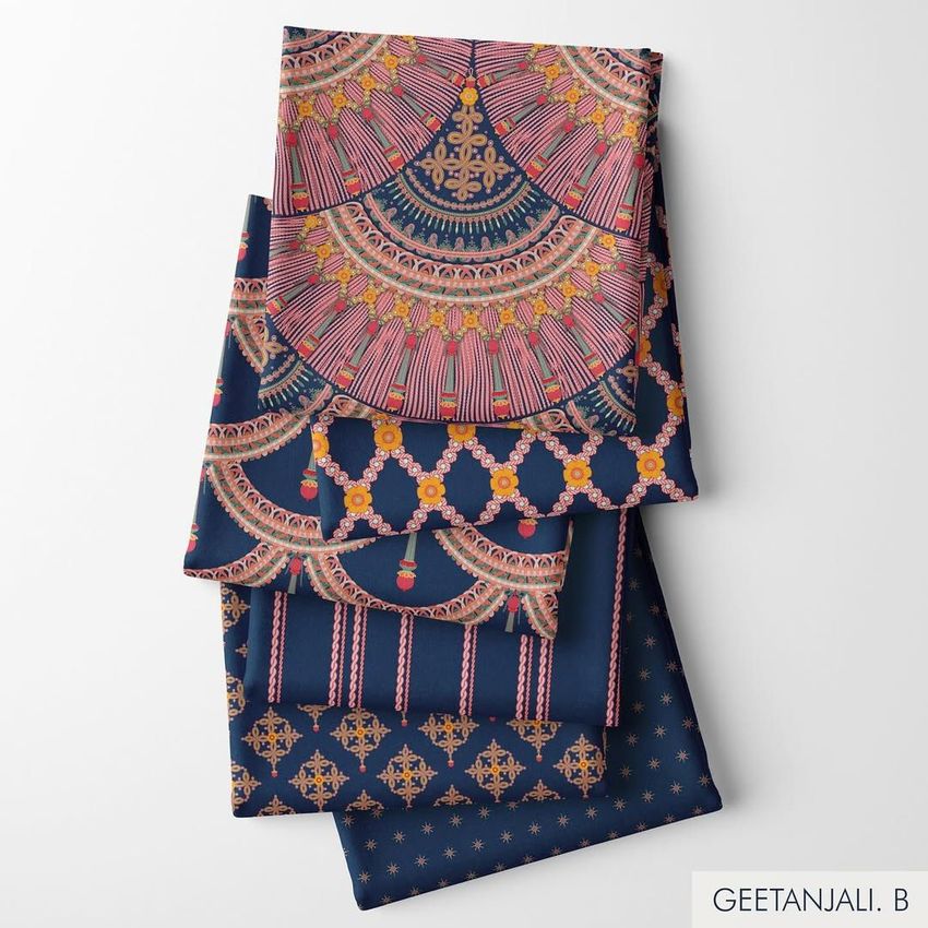 Folded fabrics mockup featuring four stacked textiles with intricate gold and pink patterns on a dark blue background, viewed from above.