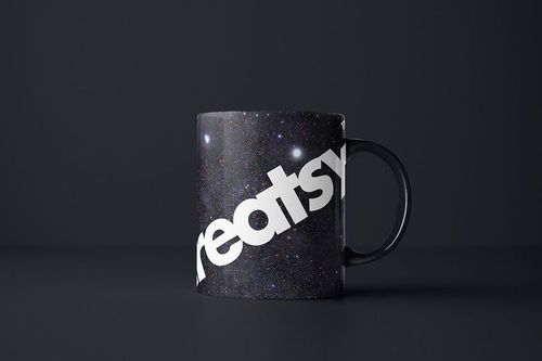 PSD mockup of a mug with a cosmic night sky print and prominent white text, displayed on a matte black tabletop.