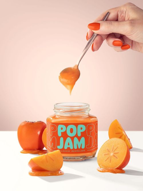 Front view of a persimmon jam jar mockup with vibrant orange label, surrounded by fresh persimmon slices and a hand holding a spoon.