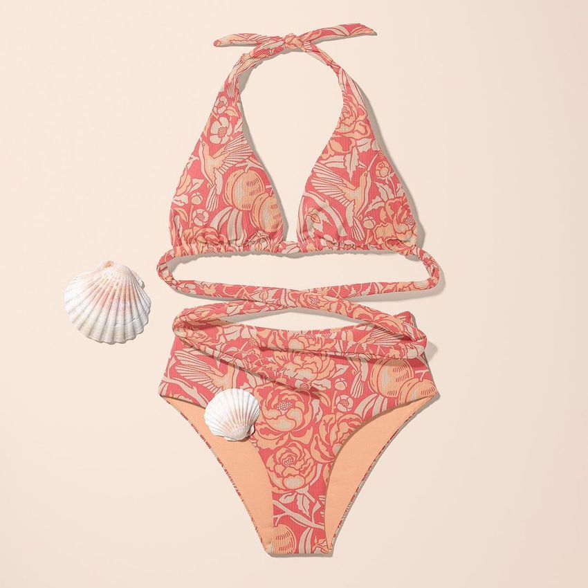High waisted bikini mockup with a pink and cream floral pattern, displayed flat on a beige background with two seashell props.