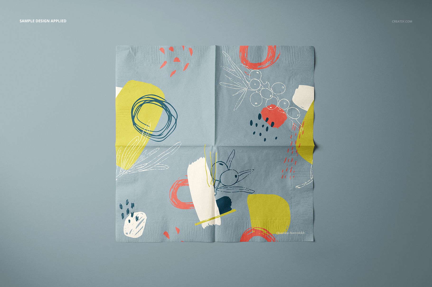 Square paper napkin mockup with abstract colorful patterns in yellow, red, and white on a light blue background, top view.