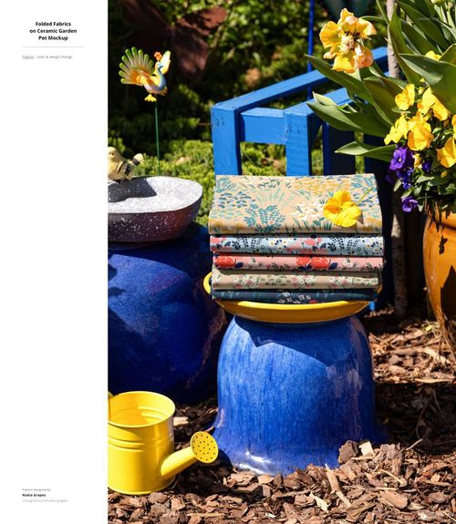 PSD mockup showing folded fabrics with various designs arranged on a blue stool, with garden tools and potted plants nearby.