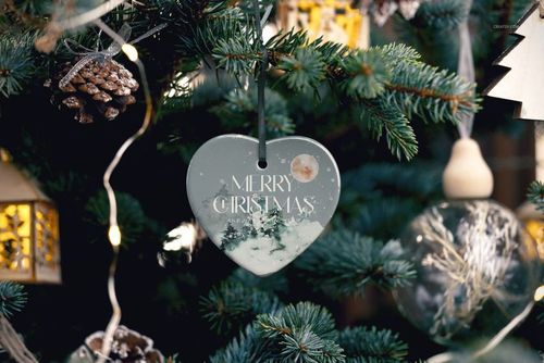 PSD mockup of a heart-shaped ceramic ornament with a holiday scene, surrounded by lights and pine cones on a tree.
