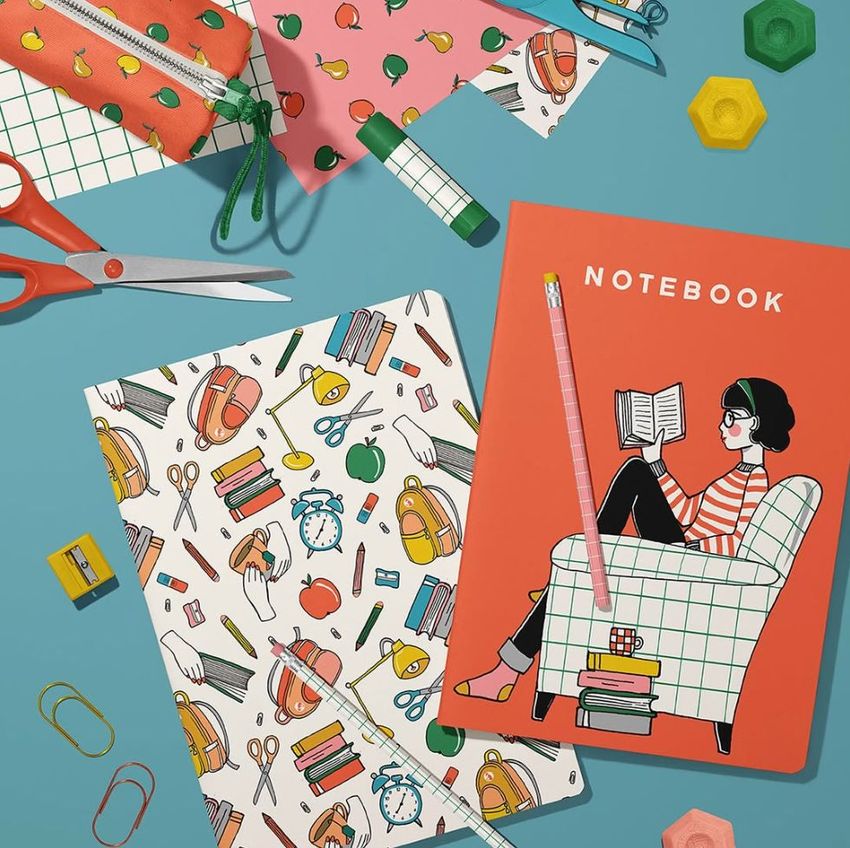 Stationery mockup featuring two classic A4 notebooks on a blue surface, surrounded by scissors, paper clips, and patterned pouches.