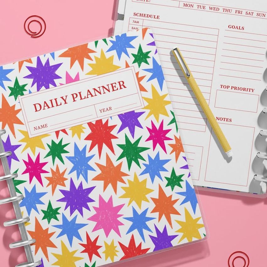 Spiral planner mockup showing a closed planner with multicolored stars and an open planner displaying lined sections and a pen.